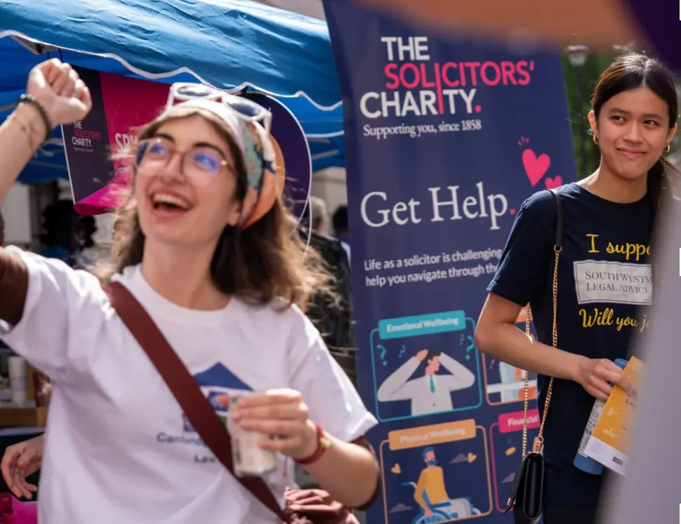 two young women standing next to the solicitors charity pop up banner looking happy.